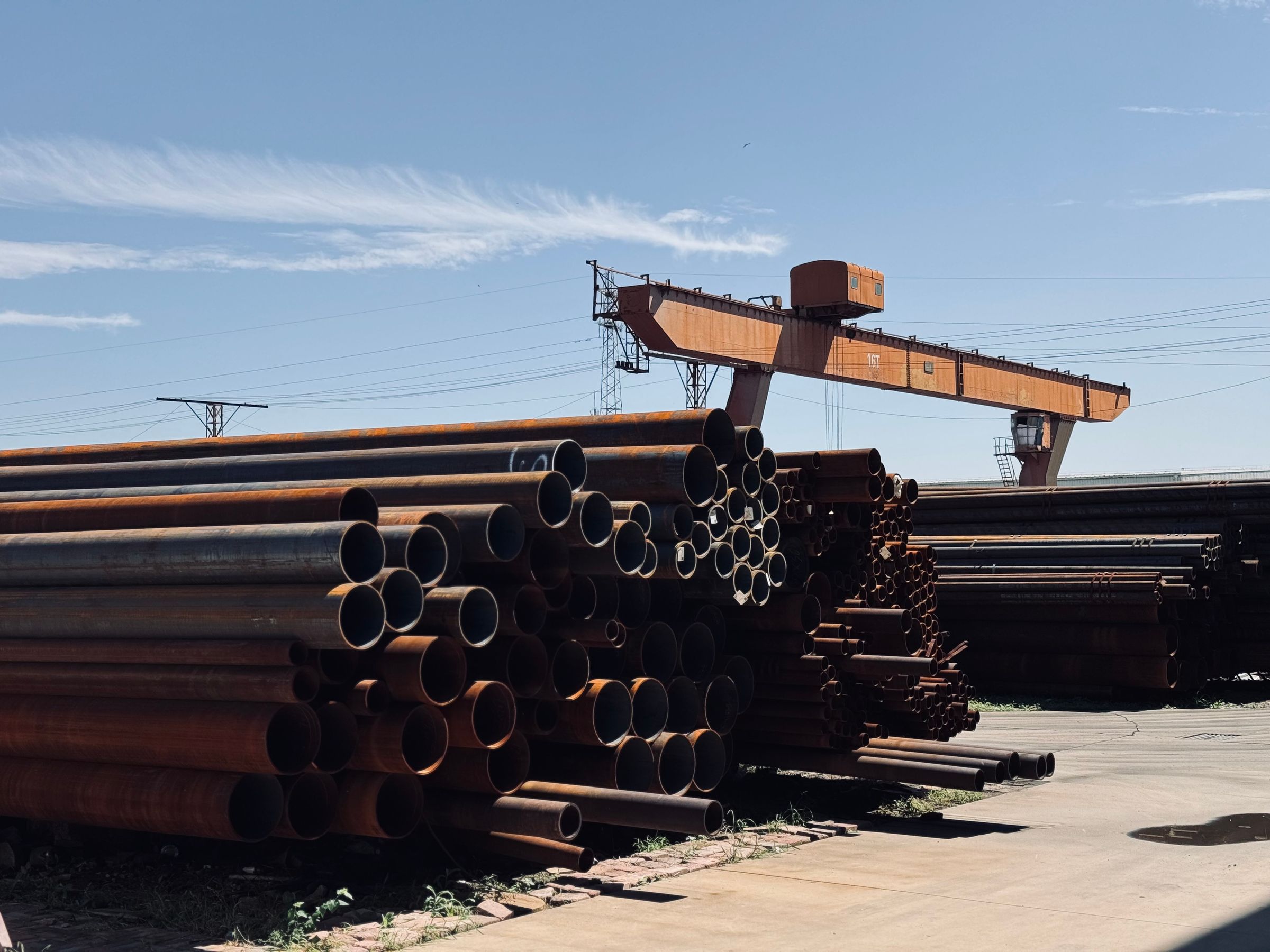 Stacked steel pipe in a pipe yard beneath an overhead crane