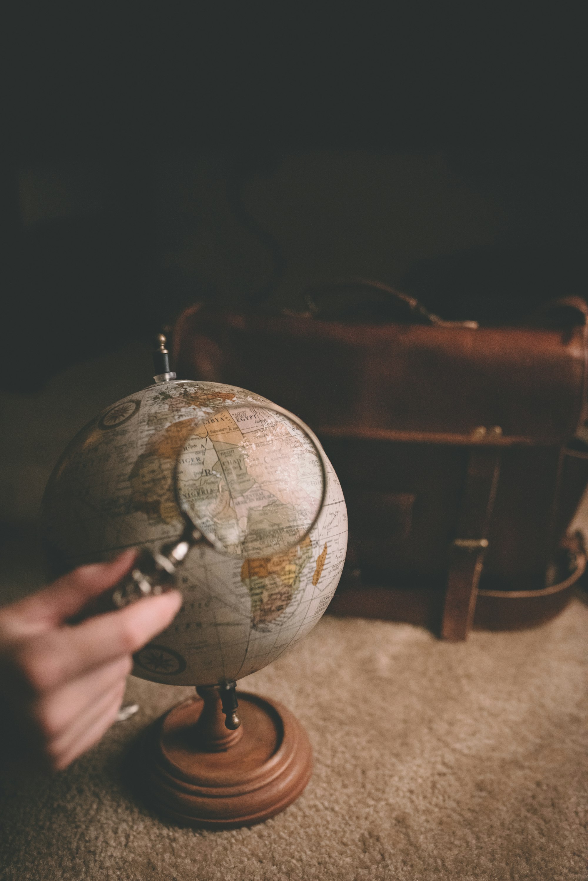 Hand holding a magnifying glass over a globe